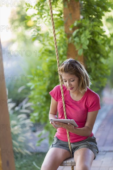 Mixed race woman using digital tablet on swing