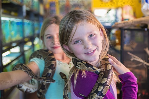 Caucasian girls playing with snakes in pet store