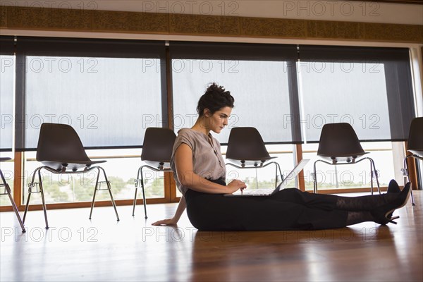 Mixed race businesswoman using laptop on floor of meeting room