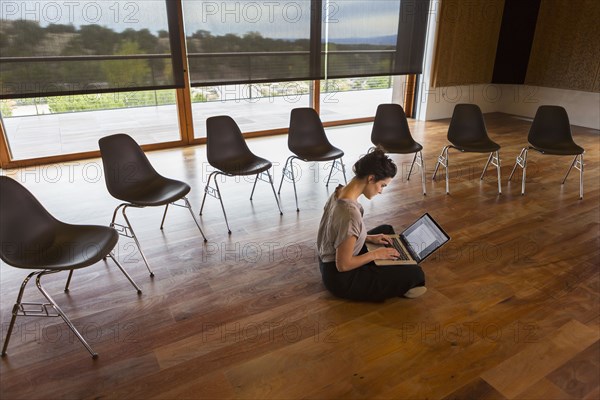 Mixed race businesswoman using laptop on floor of meeting room