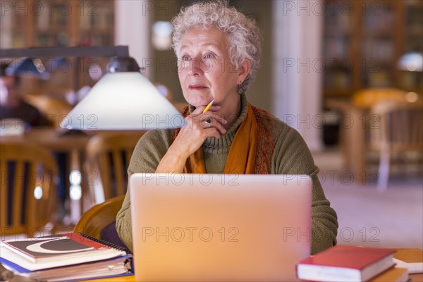 Older mixed race woman using laptop in library