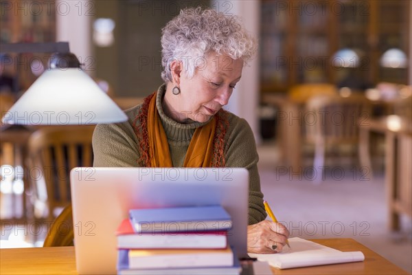 Older mixed race woman using laptop in library