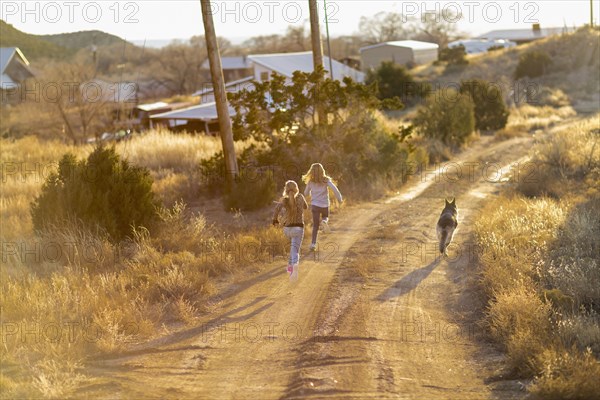 Caucasian children running on dirt road with dog