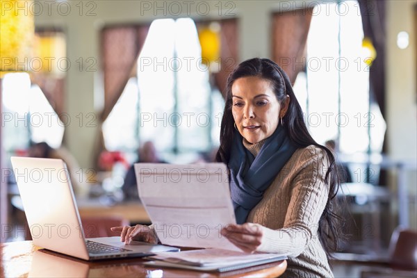 Hispanic woman paying bills on laptop in cafe