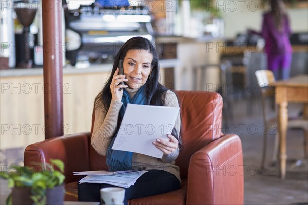 Hispanic woman paying bills on cell phone in cafe