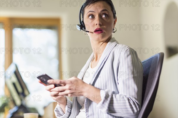 Businesswoman using cell phone and headset in office