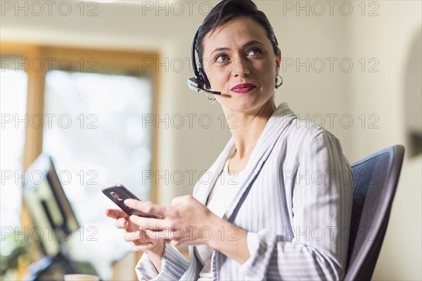 Businesswoman using cell phone and headset in office