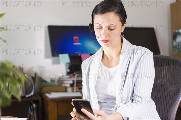 Businesswoman using cell phone and headset in office