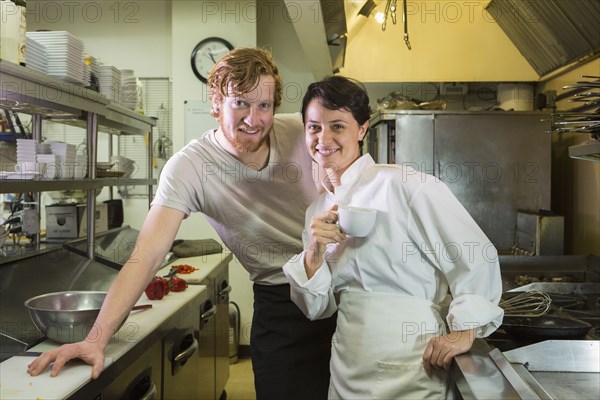 Caucasian chef and waiter smiling in restaurant kitchen