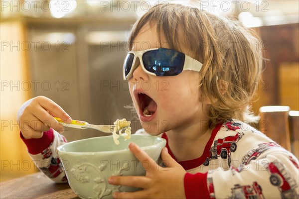Caucasian boy in sunglasses eating in kitchen