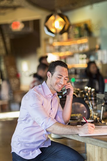 Hispanic businessman talking on cell phone in coffee shop