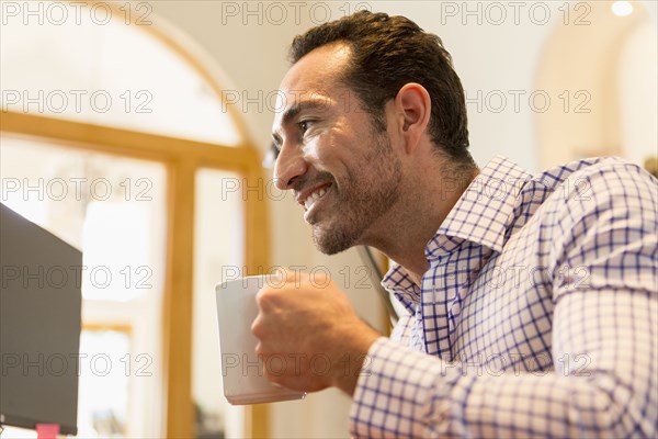 Hispanic businessman drinking coffee in office