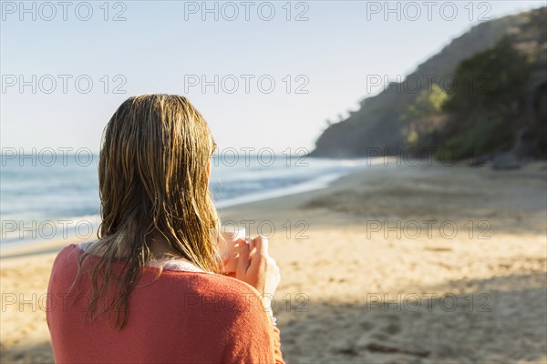 Caucasian woman drinking coffee on beach