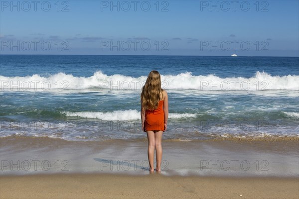 Caucasian girl standing looking at ocean waves