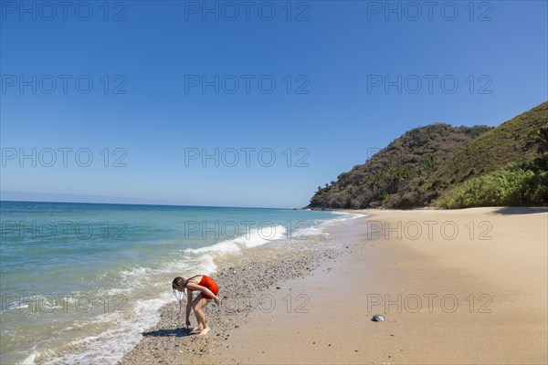 Caucasian girl examining rocks at ocean beach