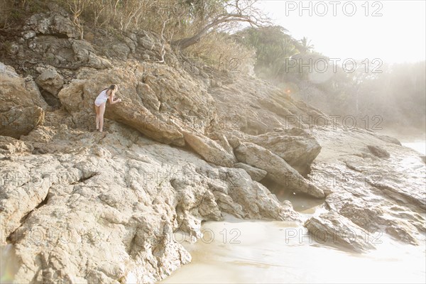 Caucasian girl climbing rocks at beach