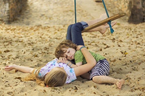 Caucasian boy laying on chest of sister at beach