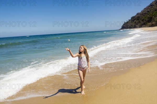 Caucasian girl tossing rock at beach