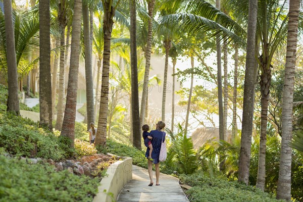 Caucasian mother carry son on path  with palm trees