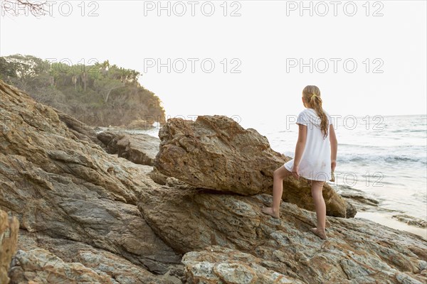 Caucasian girl climbing rocks at beach