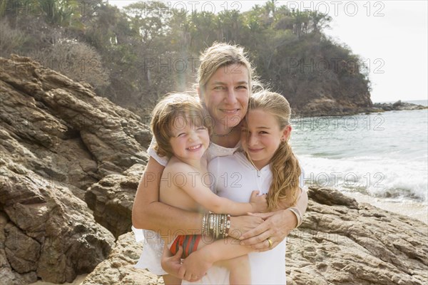 Caucasian mother hugging son and daughter at beach