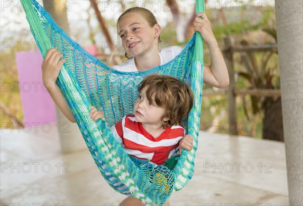 Caucasian boy sitting in hammock held by sister