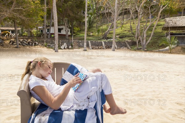 Caucasian girl sitting in beach chair playing game