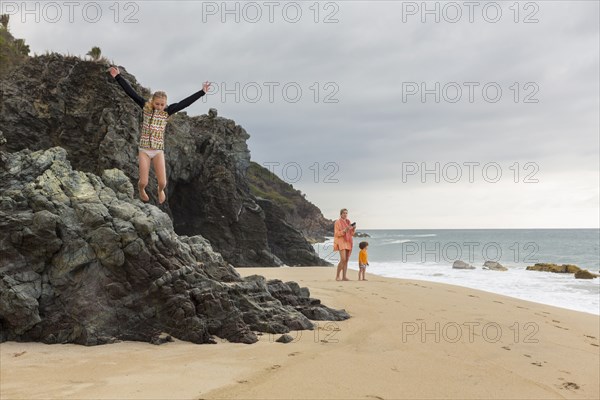 Caucasian girl jumping off rocks at beach