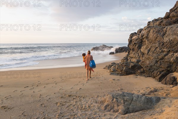 Caucasian mother carrying son on beach