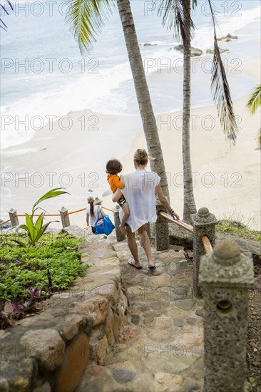 Caucasian mother carrying son descending staircase to beach