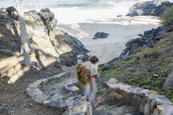 Caucasian girl carrying brother descending staircase to beach