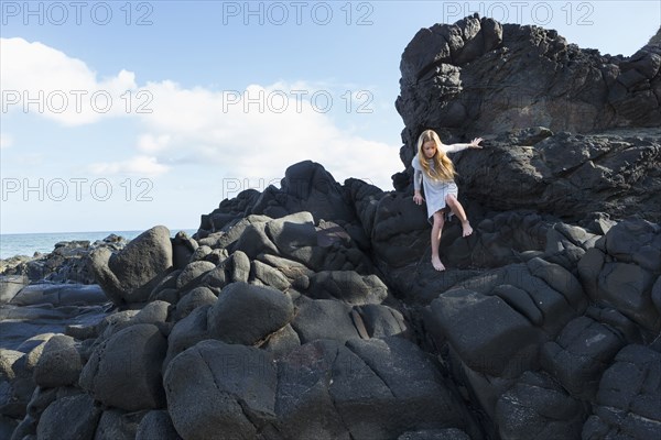 Caucasian girl climbing rocks at beach