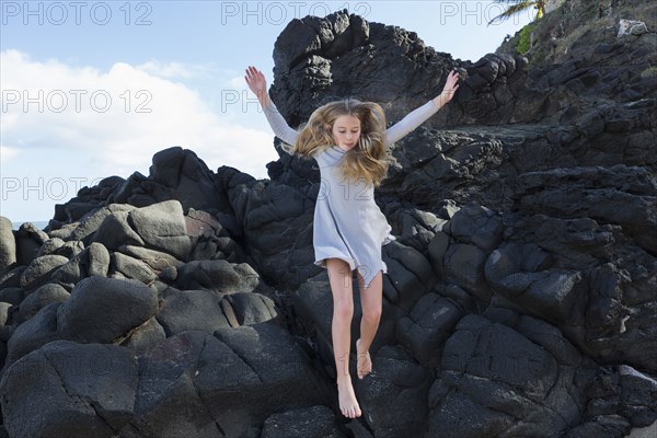 Caucasian girl jumping off rocks at beach