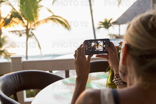 Caucasian woman photographing sunset at beach