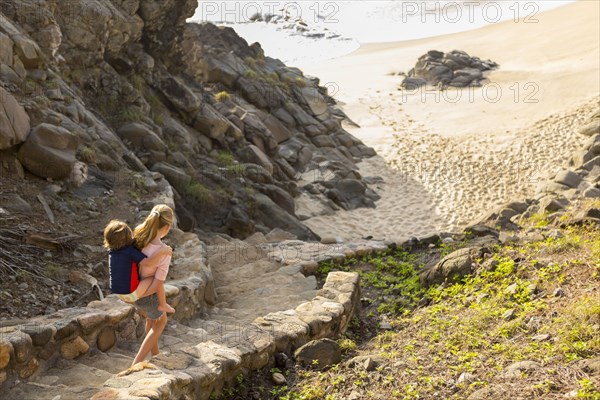 Caucasian sister carrying brother descending staircase to beach