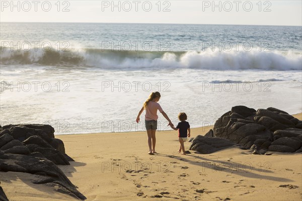 Caucasian brother and sister holding hands on beach