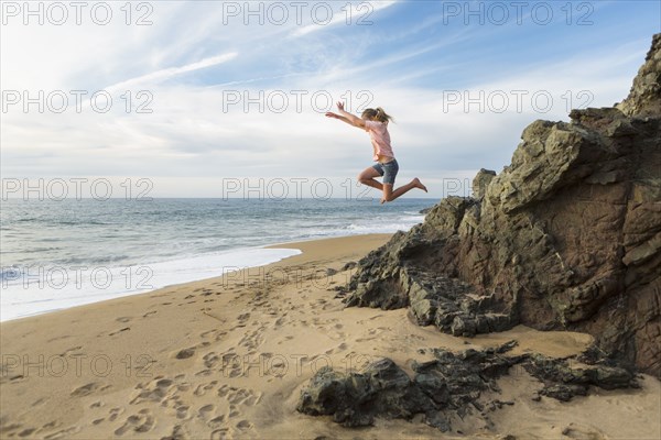 Caucasian girl jumping off rocks at beach