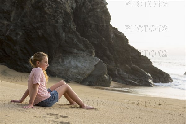 Caucasian girl sitting near rocks at beach