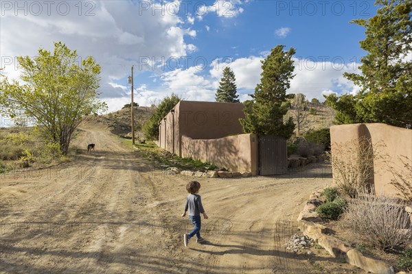 Caucasian boy walking on dirt road toward gate