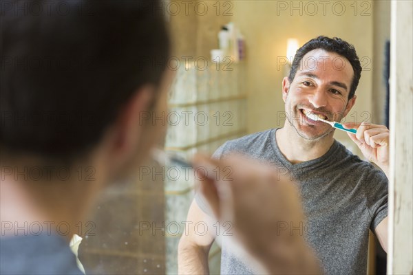 Hispanic man brushing teeth in mirror