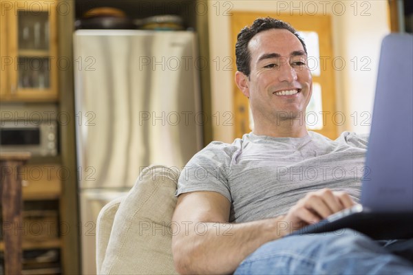 Hispanic man laying on sofa using laptop