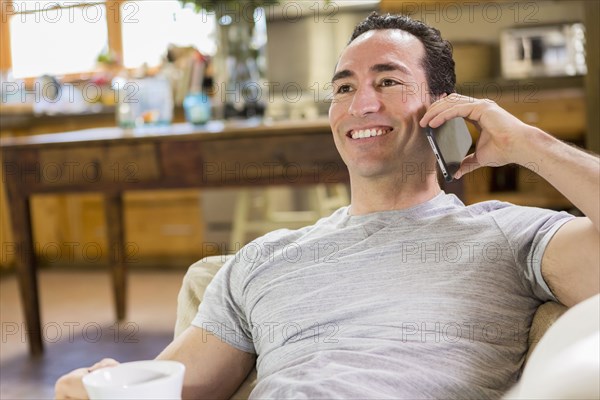 Hispanic man laying on sofa using cell phone