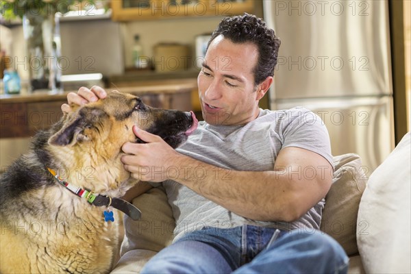 Hispanic man laying on sofa petting dog