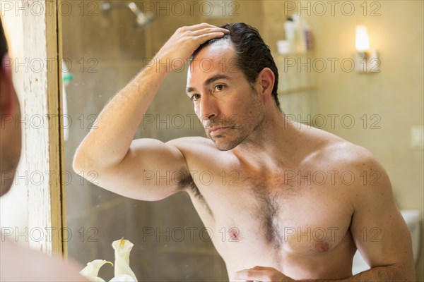 Hispanic man checking receding hairline in mirror