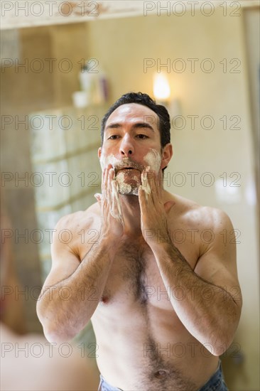 Hispanic man applying shaving cream to face in mirror