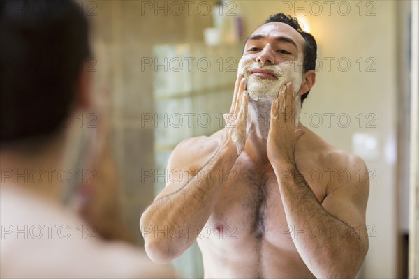 Hispanic man applying shaving cream to face in mirror