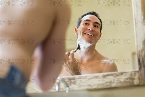 Hispanic man using razor to shave face in mirror