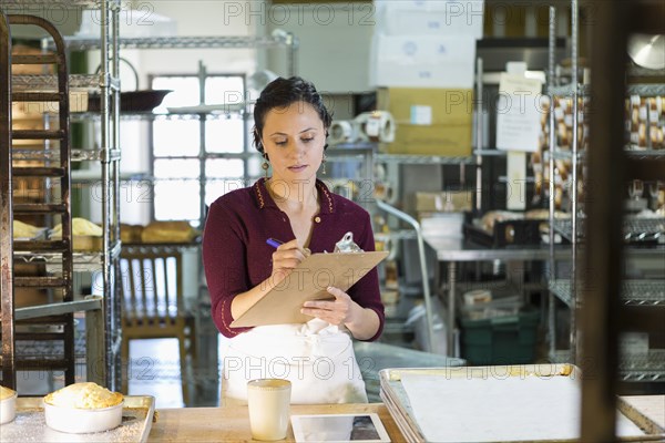 Caucasian woman writing on clipboard in bakery