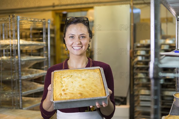 Caucasian woman showing cake in bakery pan