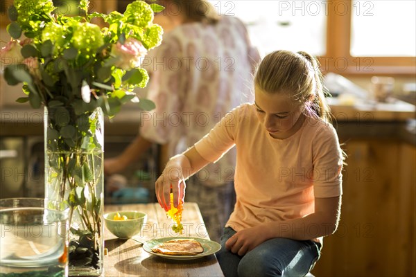 Caucasian girl squeezing honey from bottle onto pancake